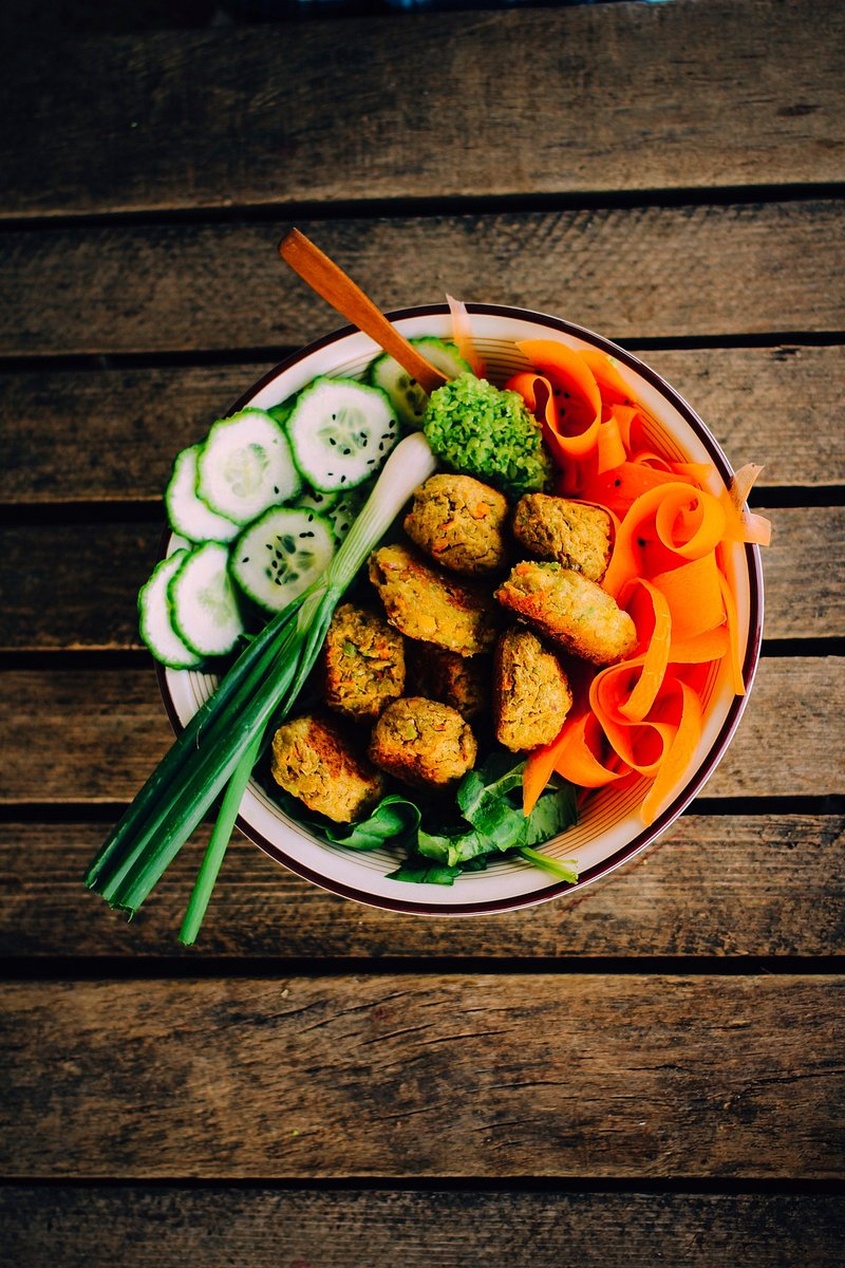 En vackert arrangerad skål med gyllene falafel, gurka, morot och broccoli som visar en komplett växtbaserad måltid.
