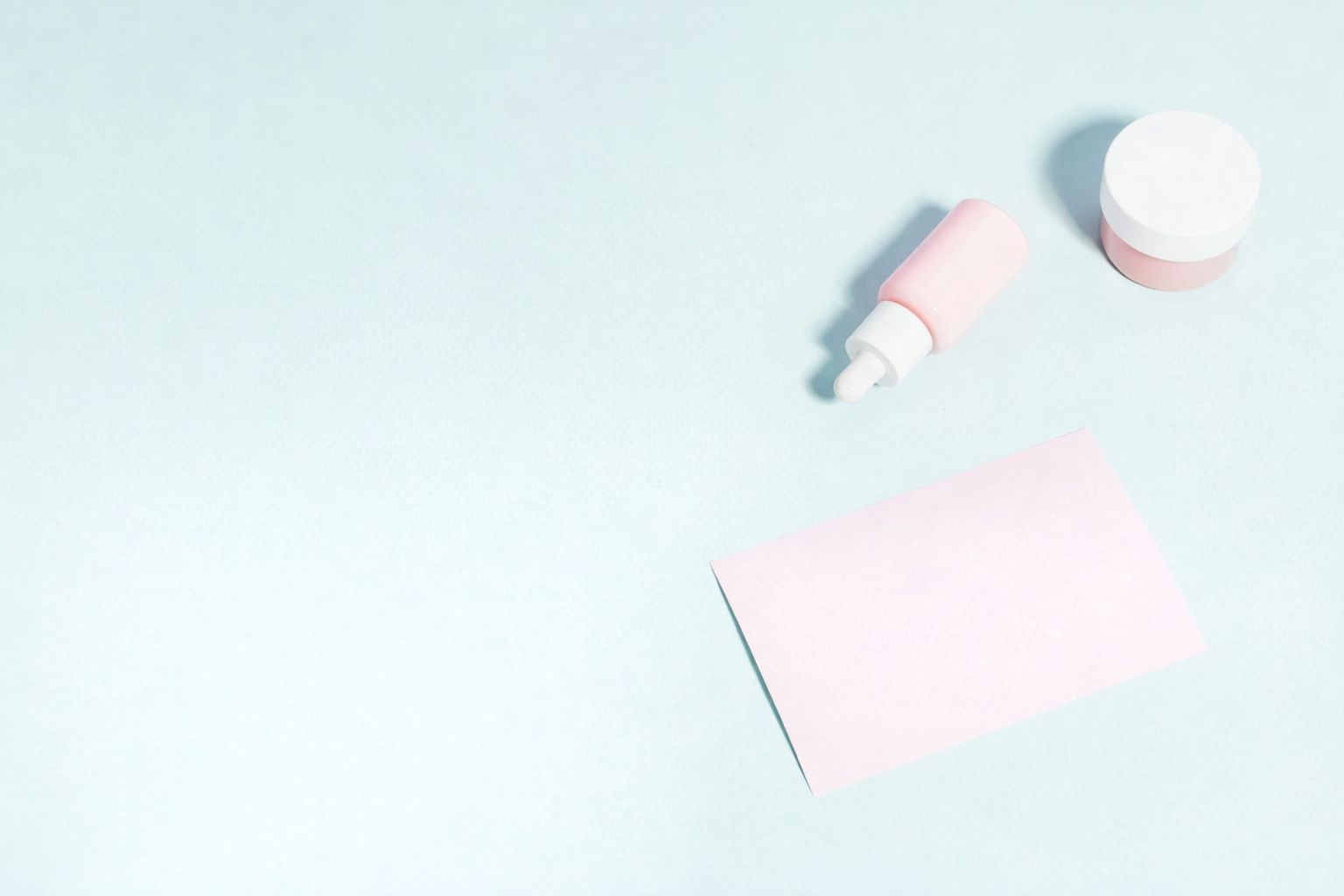 Rosa hudvårdsprodukter och anteckningskort på ljusblå bakgrund, för marknadsföring.