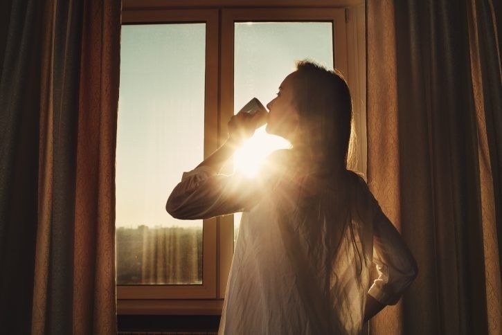 Person dricker ur en kopp i morgonljus vid ett fönster