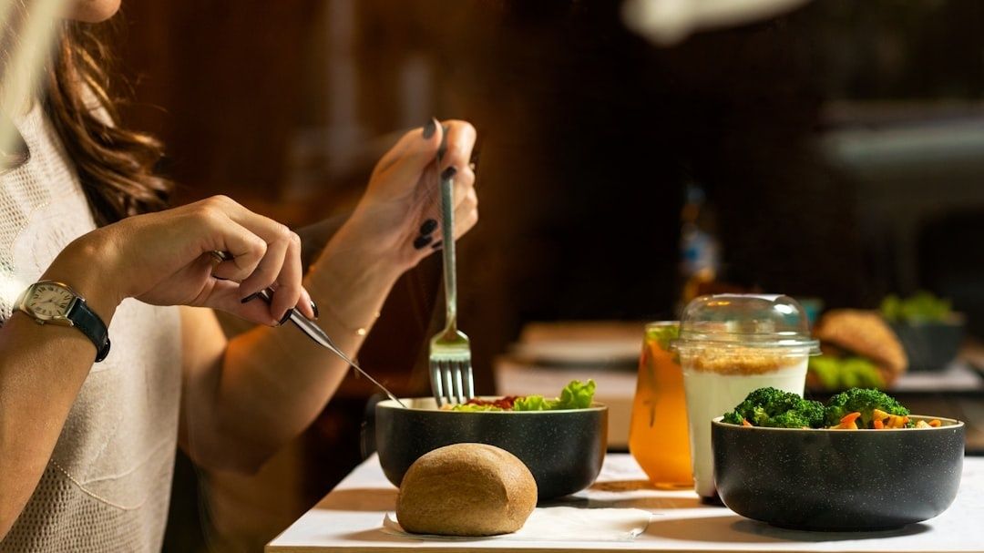 Person äter en måltid med sallad, bröd och grönsaker vid ett dukat bord